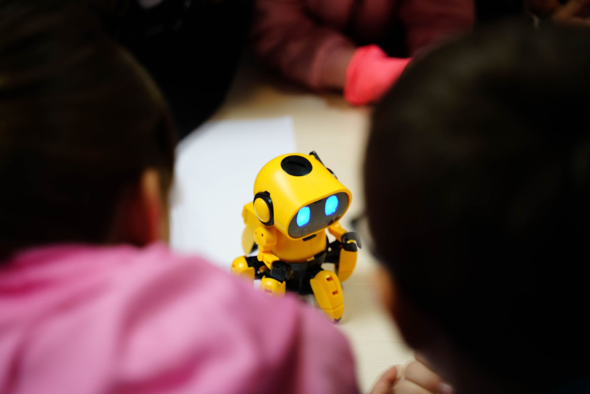 A yellow toy robot captivates two children in a classroom setting, fostering engagement and learning.