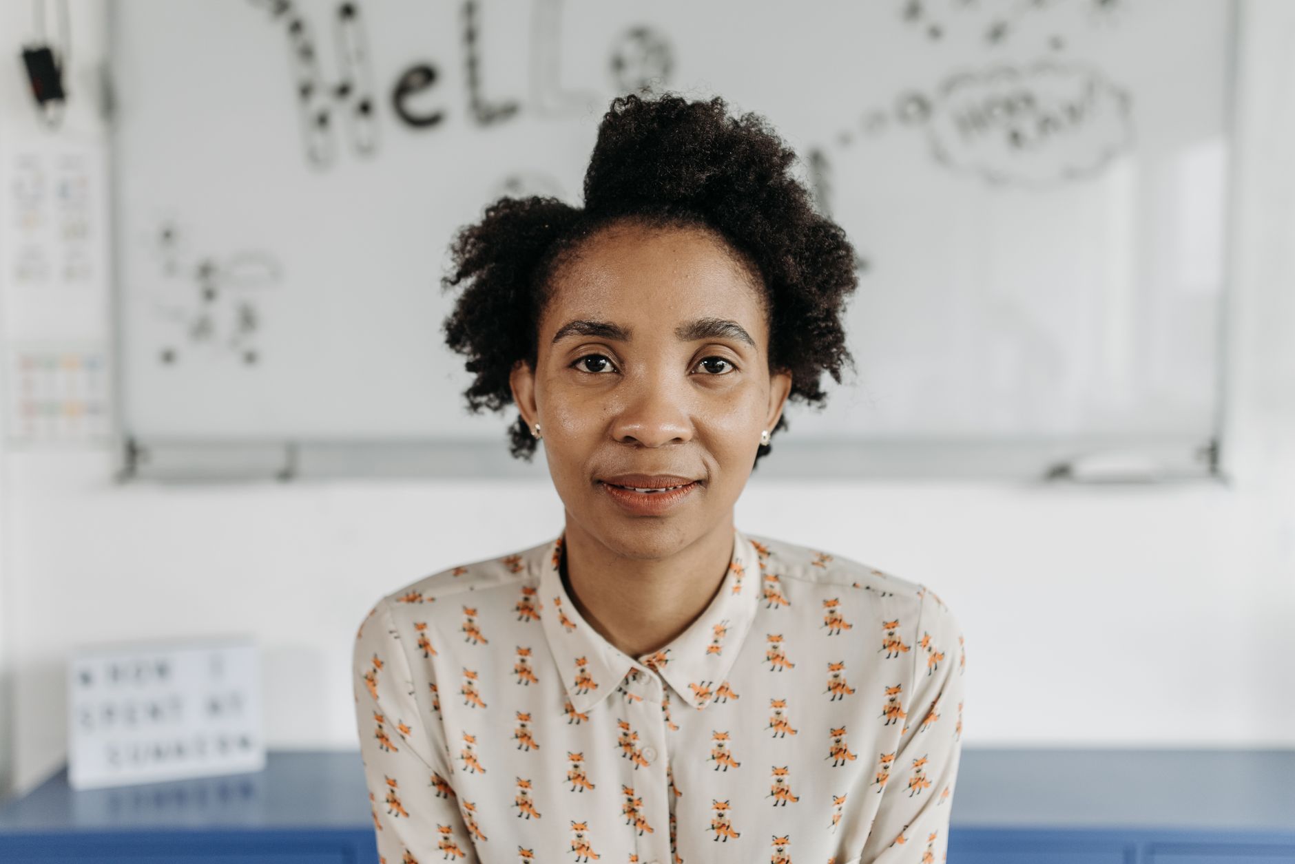 A confident woman with afro hair poses in a classroom, fostering an educational theme.