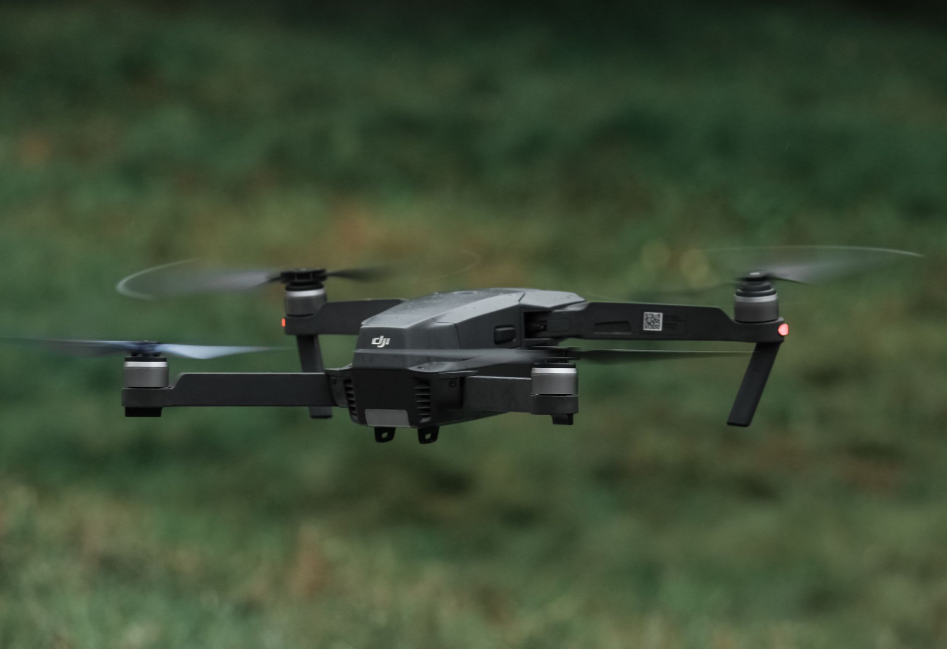 A drone in flight outdoors, showcasing its sleek design and spinning rotors.