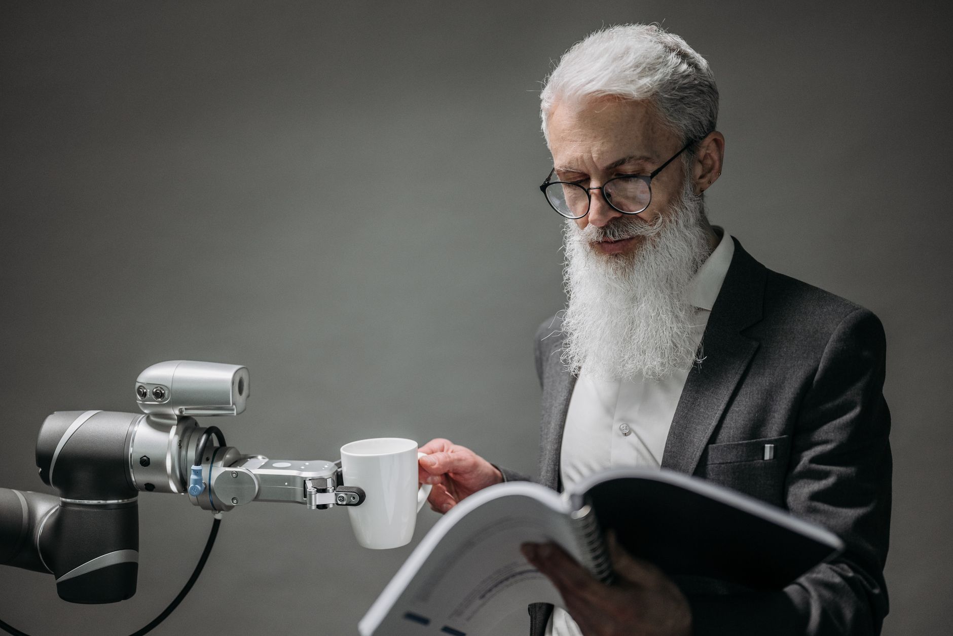 Senior man interacts with robotic arm and cup in a modern studio environment.