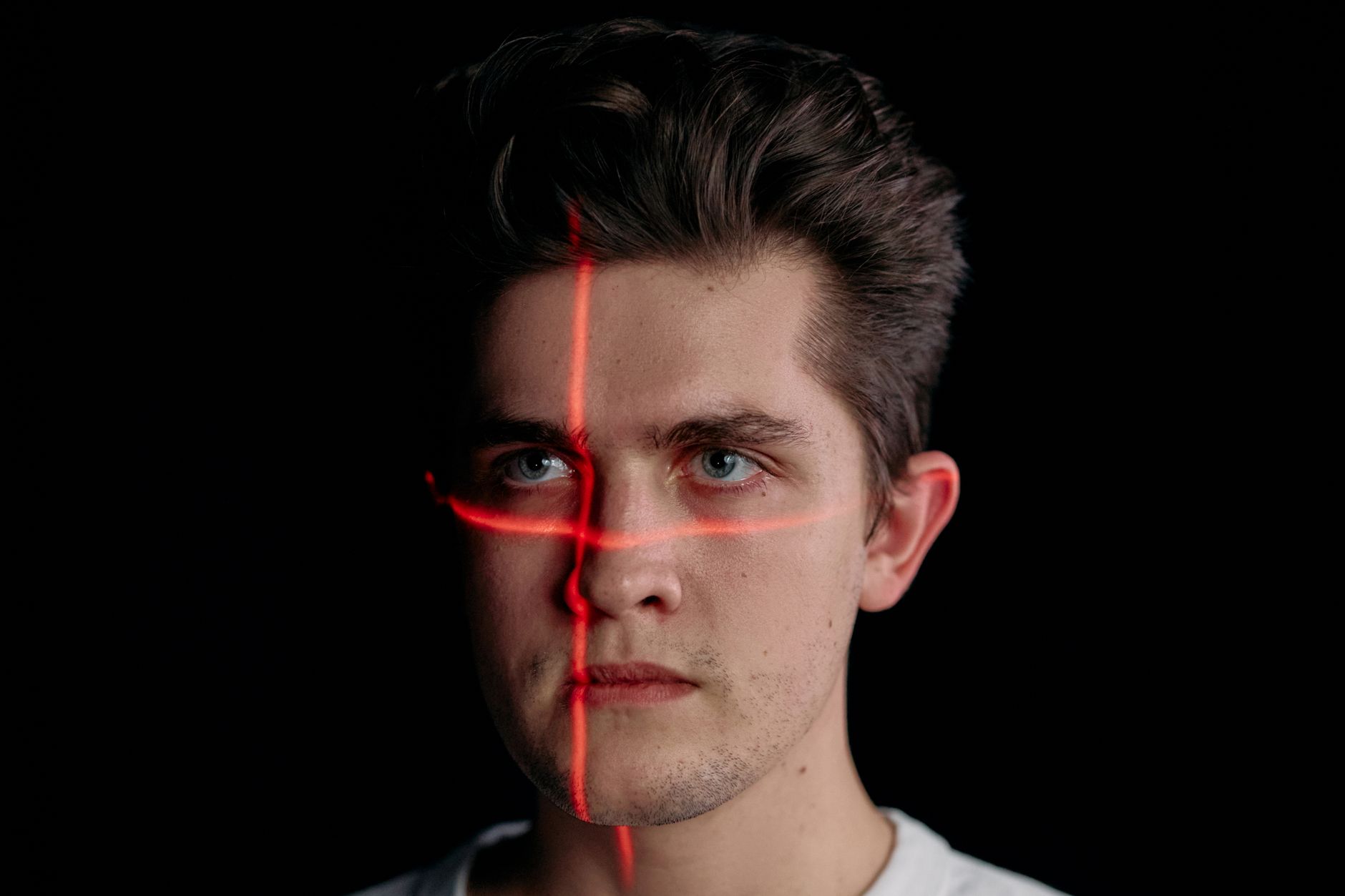 Conceptual portrait with laser scanning for facial recognition on plain black background.