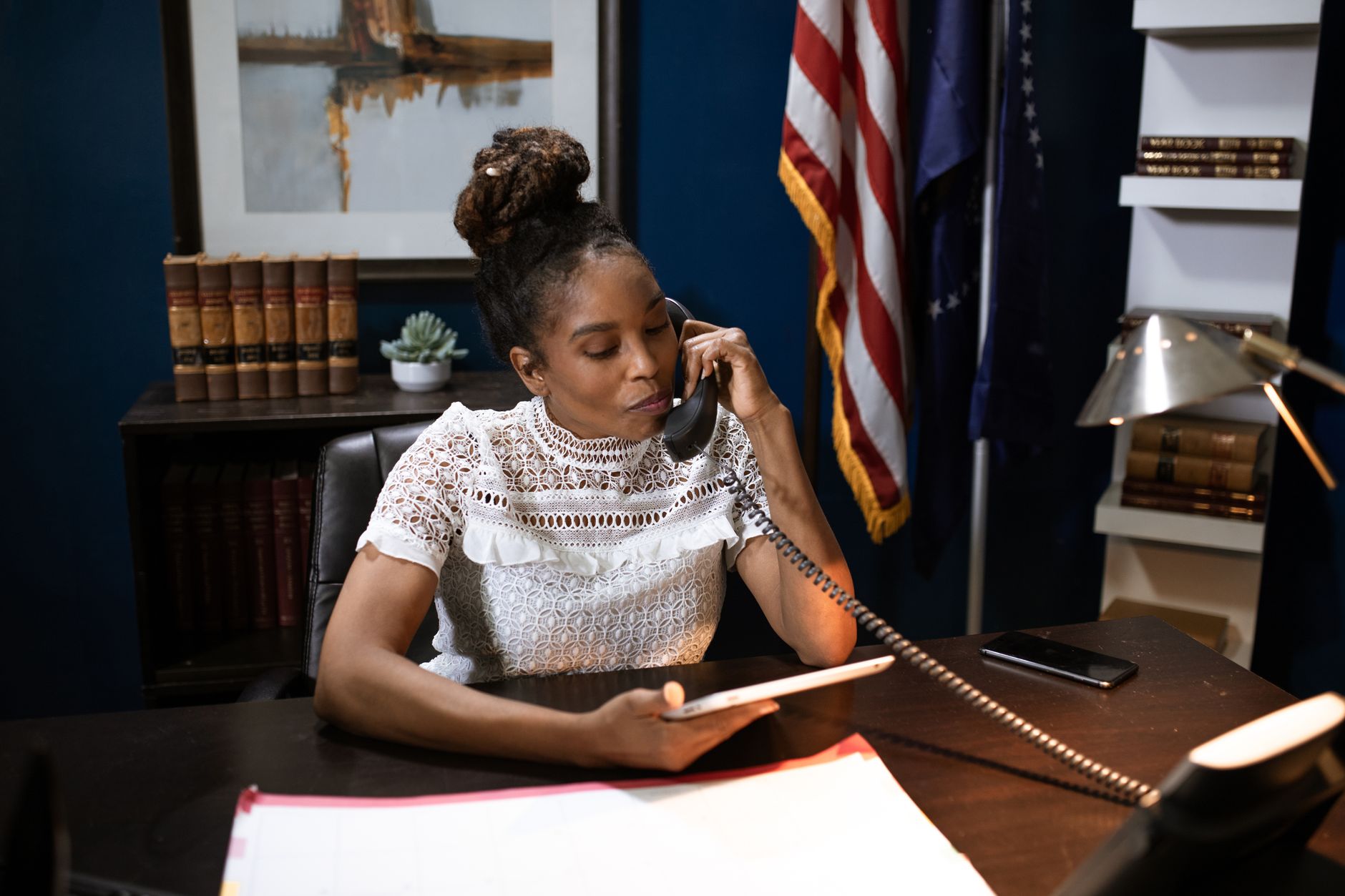 Businesswoman multitasking with phone and tablet at desk in office setting.