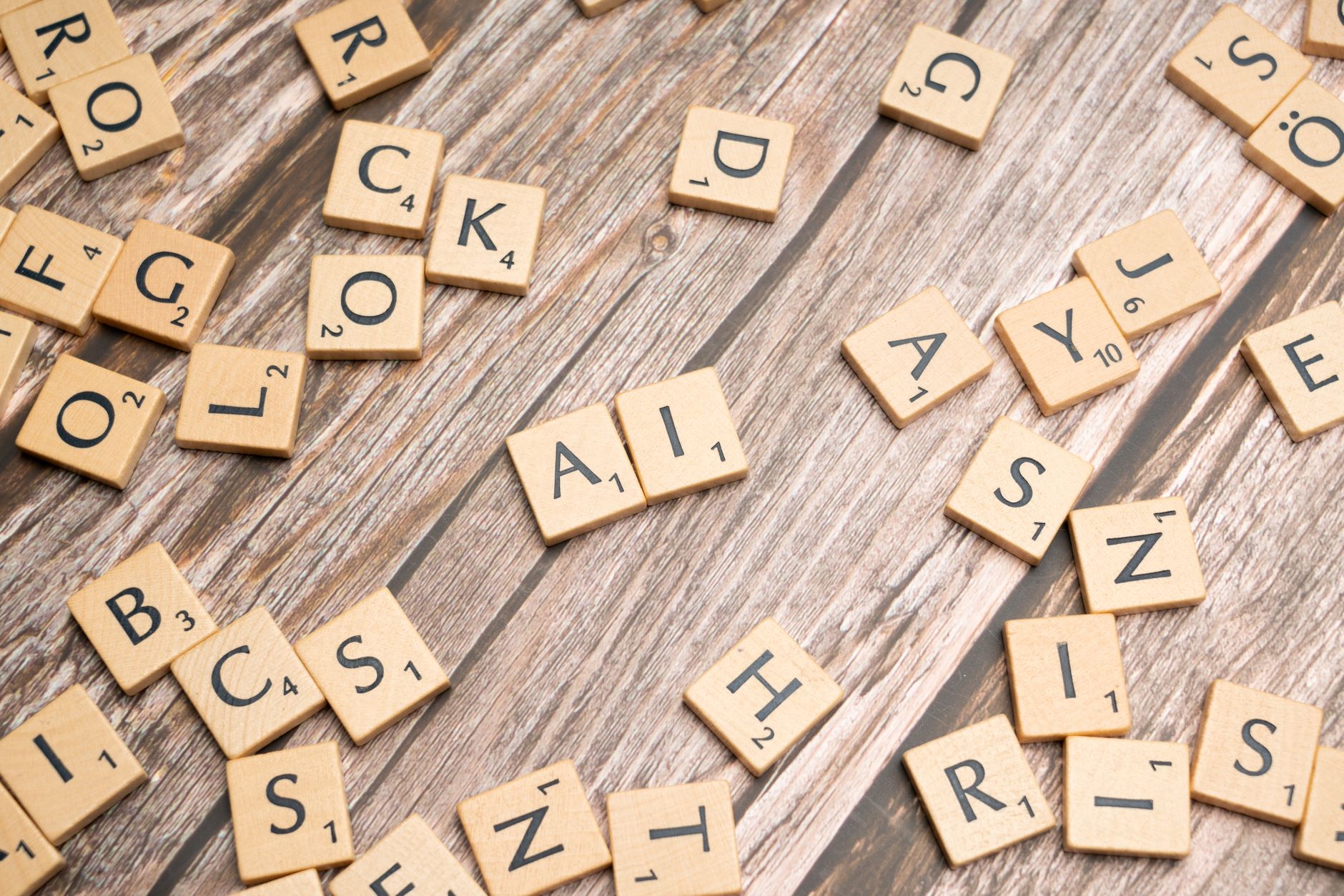Wooden letter tiles scattered on a textured surface, spelling 'AI'.