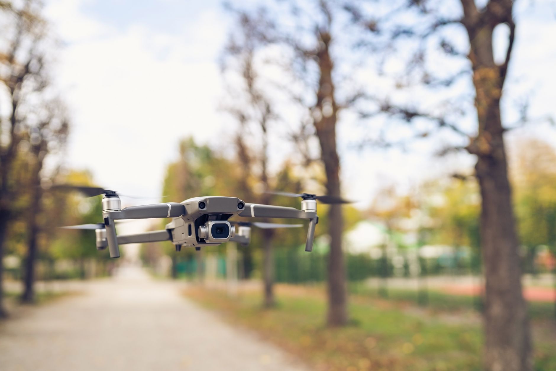 Close-up of a drone hovering along a tree-lined pathway in fall.