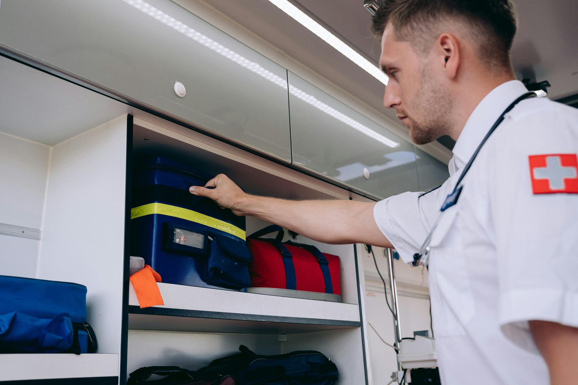 A paramedic organizes medical supplies inside an ambulance shelf for emergency preparedness.