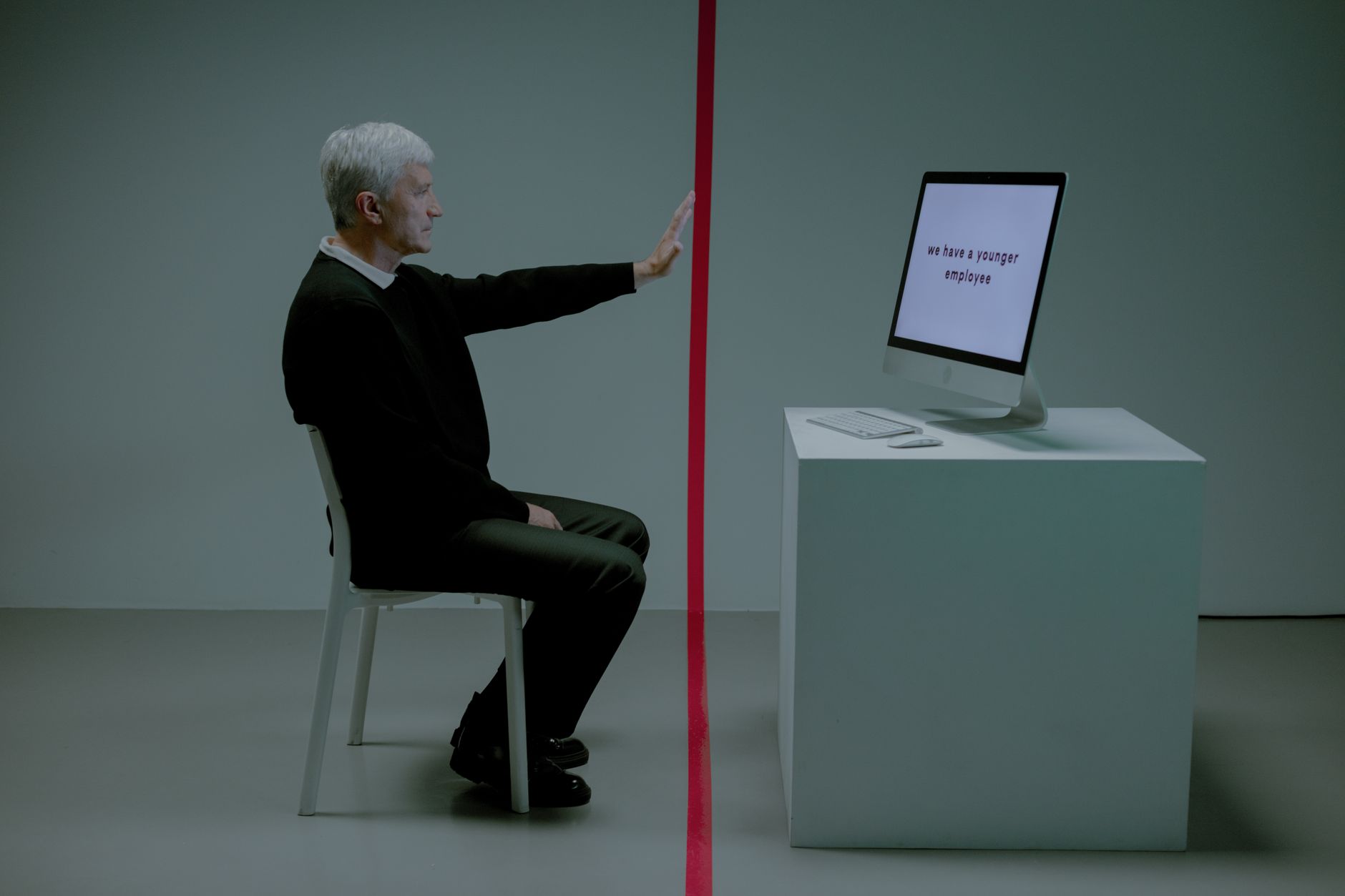 Senior man facing age discrimination in workplace, seated opposite a computer.