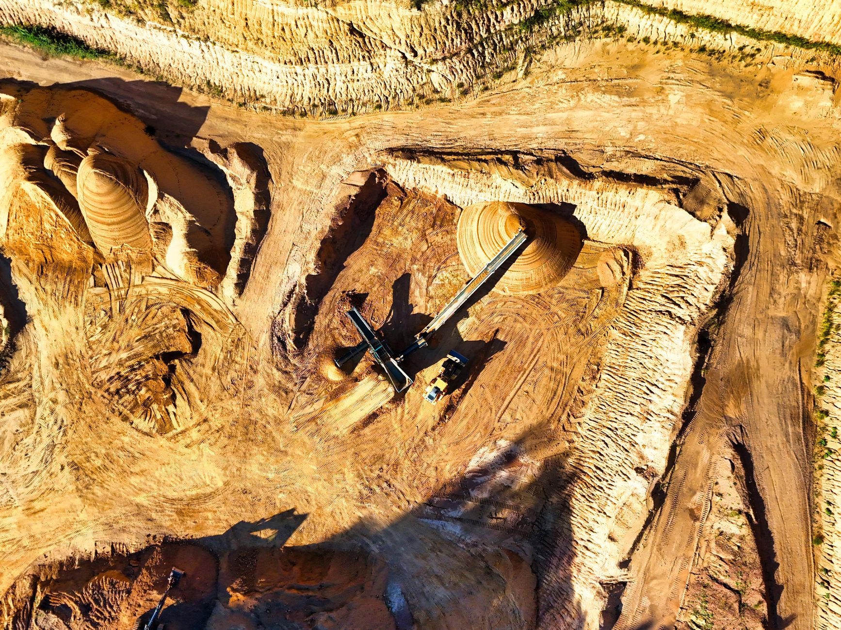 Aerial shot of a vast open-pit mine with visible heavy machinery excavating minerals.