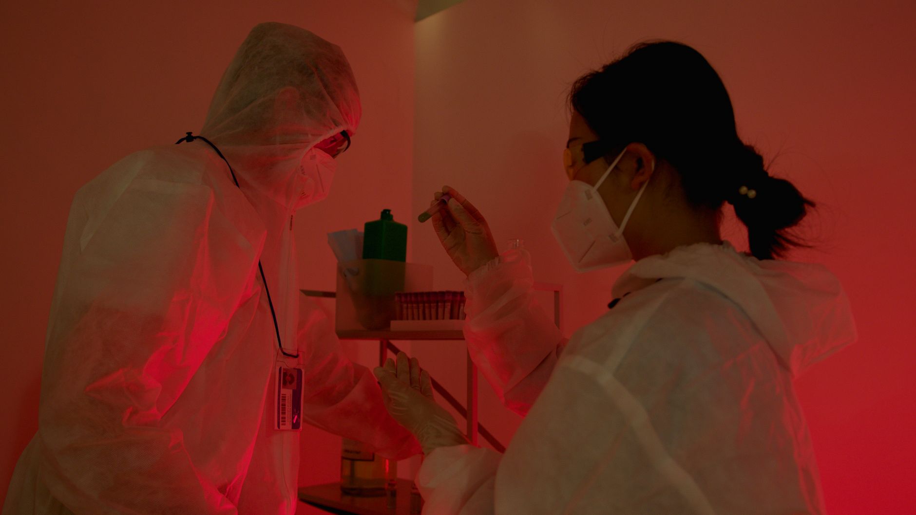 Scientists in protective gear working in a lab lit by red light, conducting experiments safely.
