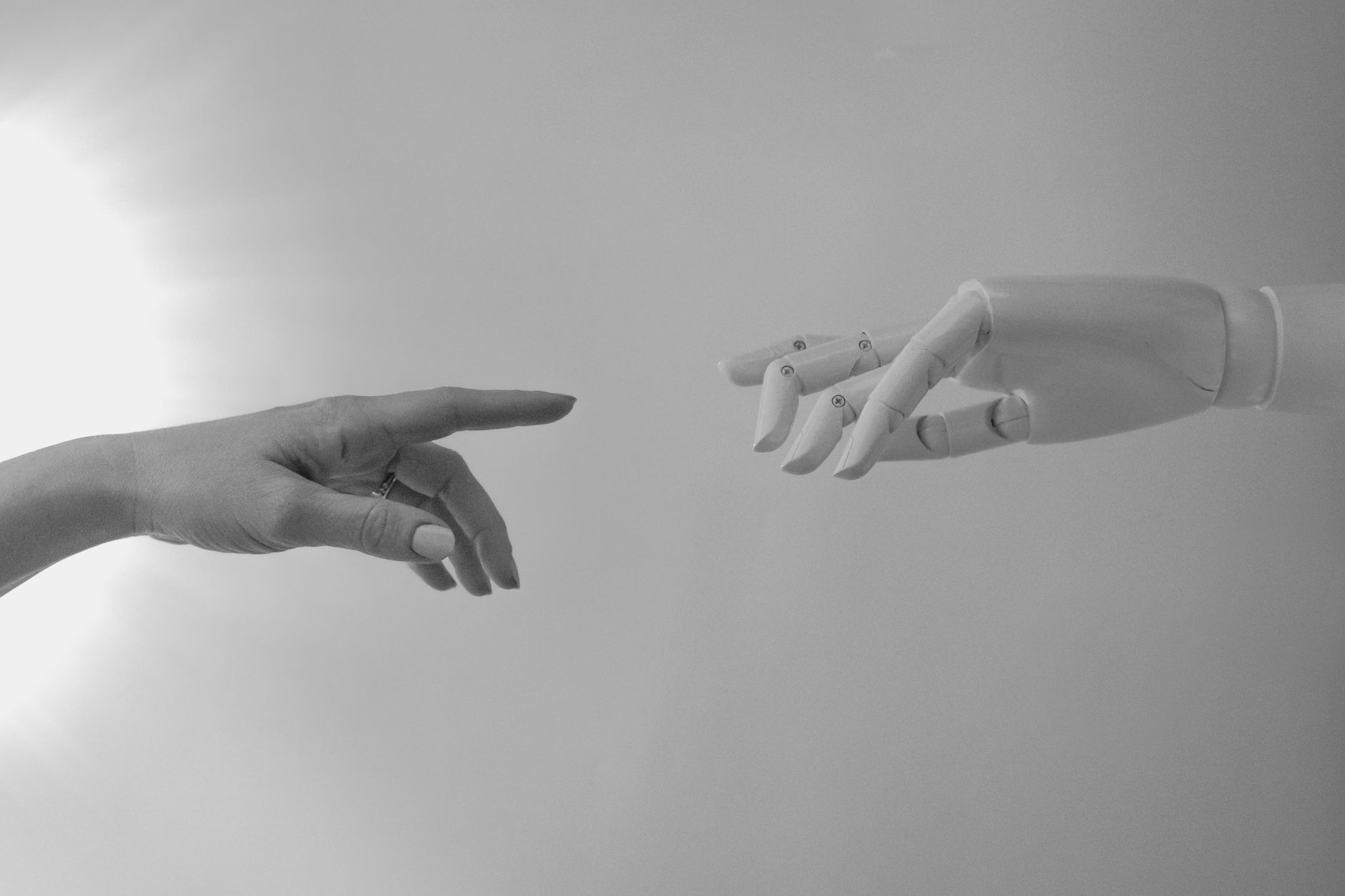 Black and white image of a human and robotic hand reaching towards each other, symbolizing connection.