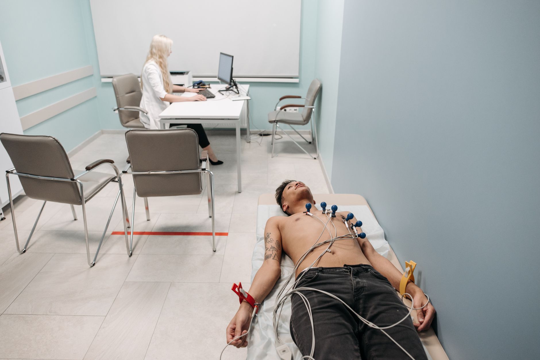 A patient undergoes a cardiogram while a doctor uses a computer in a medical clinic.